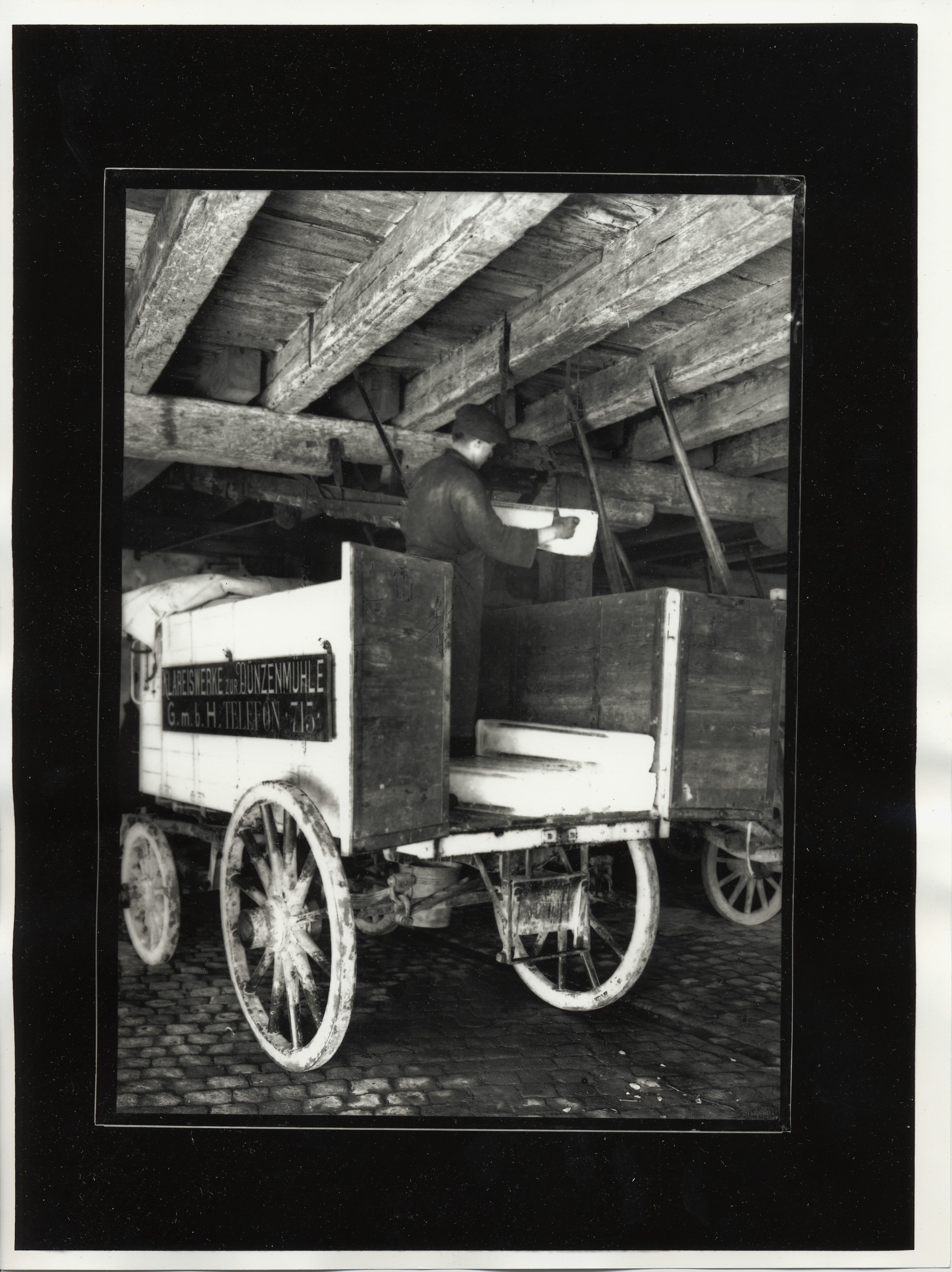 Chargement d’un chariot servant au transport des pains de glace. Ces derniers descendent du 1er étage par une glissière derrière l’ouvrier.